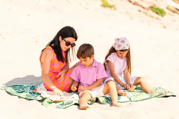Mãe e filhos na praia a fazer atividades do kit Rabiskas