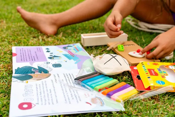 Caderno de atividades, plasticinas e jogos do kit Rabiskas pousados na relva