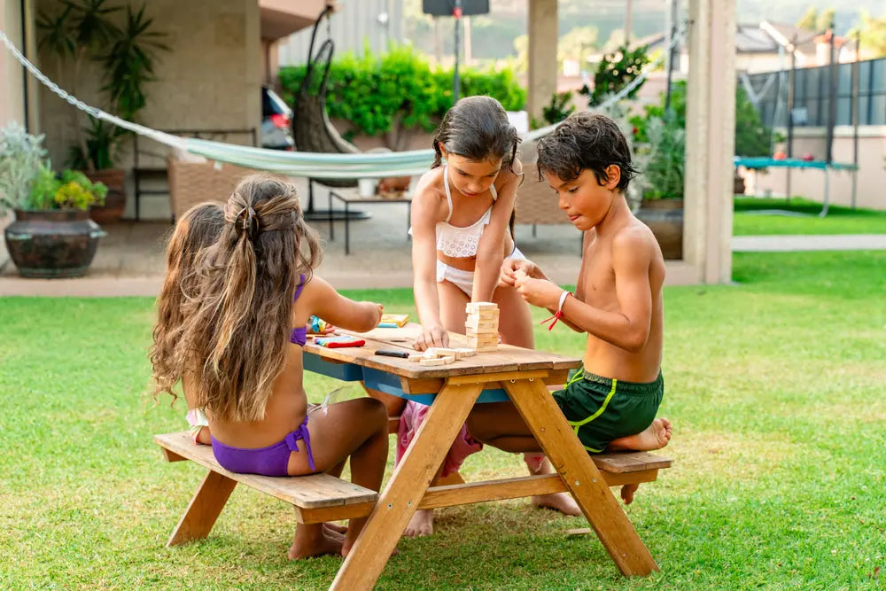 Crianças numa mesa de piquenique no jardim a jogar com o kit Rabiskas