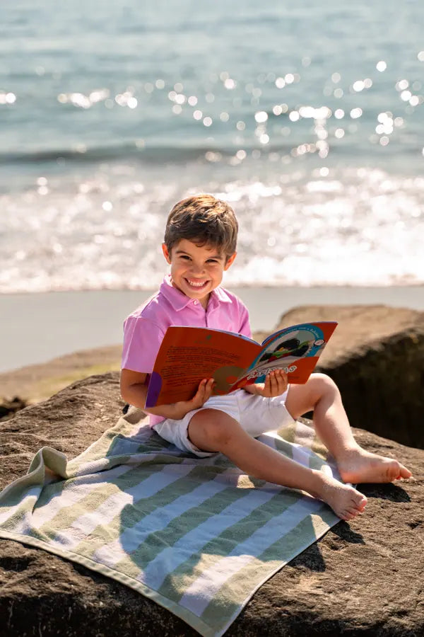 Menino na praia a ler o caderno de atividades Rabiskas